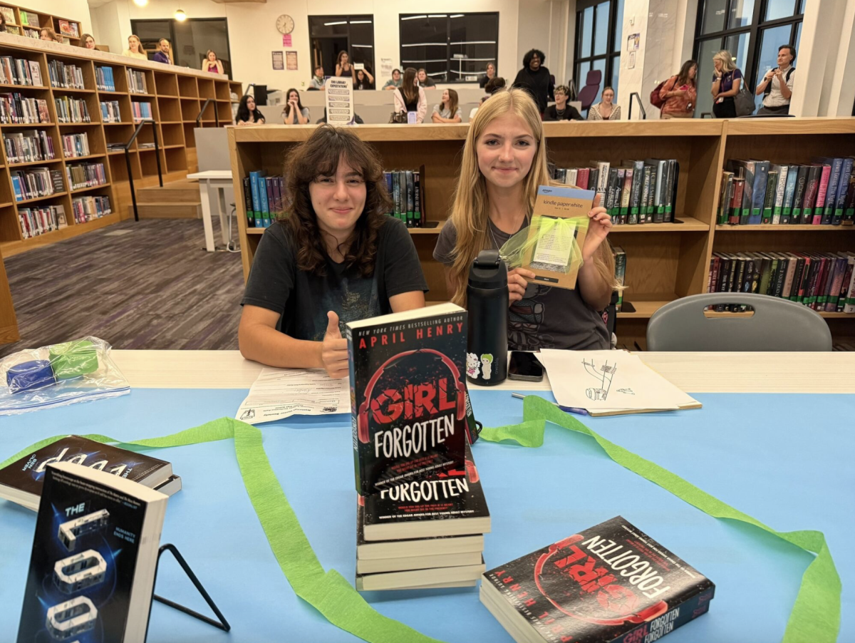 Senior Ingrid Swanson and Sophie Huffless showcasing books and a Kindle Paperwhite at Literacy Night