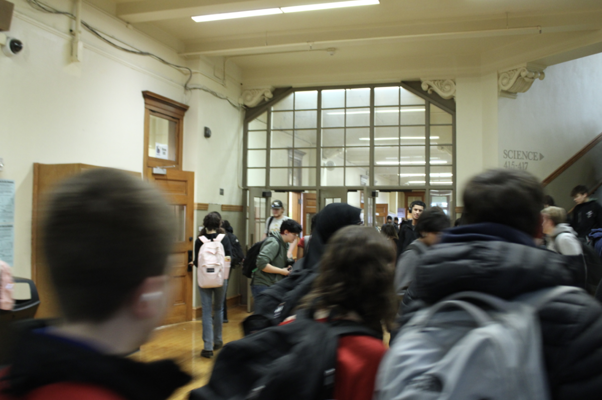 A hallway full of students walking to their classes from 1 side on the third floor looking down 1 side to 2 side